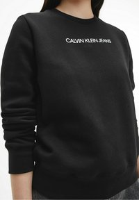 Sudadera negra de mezcla de algodón, con puños y dobladillo acanalados, con el logo "CALVIN KLEIN JEANS" en blanco en el pecho.