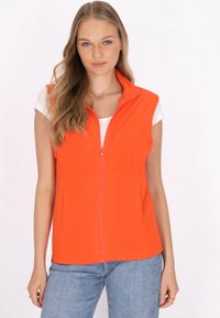 Orange ärmellose Weste mit einem Reißverschluss vorne, aus glattem Material. Mit einem hohen Kragen und einem lässigen Design, kombiniert mit einem weißen Oberteil.