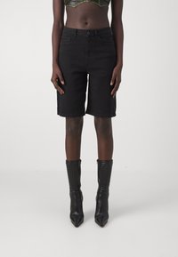 Černé denimpantalony Bermudy s volným střihem, mají pět kapsových design a zapínání na knoflík, doplněné o texturované černé kotníkové boty.