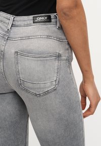 Κοντινό πλάνο ενός ατόμου που φοράει ανοιχτό γκρίζο τζιν με μαύρη ετικέτα που γράφει «ONLY» στη μέση και ορατή πίσω τσέπη.