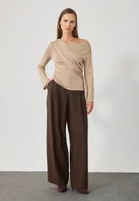 Haut beige cache-cœur à manches longues, avec un détail noué à la taille. Associé à un pantalon marron à jambes larges et des talons assortis.