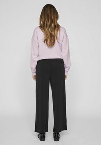 Svijetlo ljubičasti dukserica s spuštenim ramenima, u kombinaciji s labavim crnim hlačama. Glatka tekstura tkanine, dizajn punih dužina i jednostavna silueta.