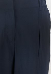 Pantaloni blu navy con una texture liscia, caratterizzati da pieghe laterali e design minimalista. Inclusi cuciture discrete e una cintura semplice.