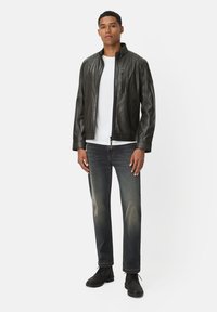 Czarna skórzana kurtka z kołnierzem, zamkiem błyskawicznym i teksturowanymi detalami. Nosi się ją na białej koszuli, w zestawieniu z ciemnymi dżinsami i czarnymi butami.