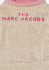 Giacca beige pelosa con colletto rosa e testo ricamato rosa "THE MARC JACOBS" sulla parte superiore della schiena.