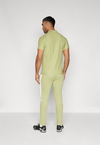 Vêtements de sport pour hommes : polo léger ajusté vert clair à manches courtes avec un jogging assorti présentant des rayures blanches sur les côtés, associé à des chaussures de sport noires.