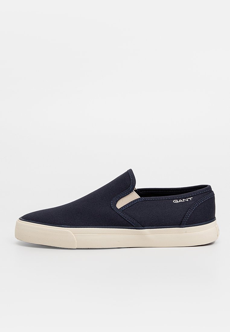 Bottines slip-on bleu marine avec semelle en caoutchouc blanche et logo GANT sur le côté, présentées sur un fond blanc uni.