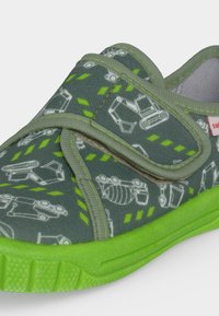 Gros plan sur une chaussure pour enfant avec une semelle verte, une tige grise, une bande Velcro et des motifs d'engins de chantier blancs avec des touches de vert.