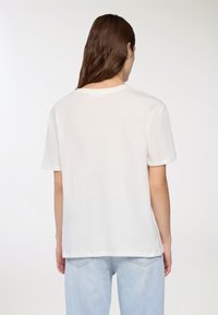 Biała bawełniana koszulka z krótkim rękawem, okrągłym dekoltem i luźnym krojem. Prosty design bez widocznych wzorów lub ozdób.