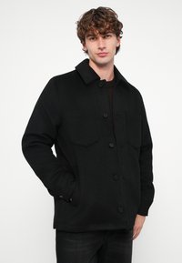 Sort uldblandet jakke med krave, knappelukning foran, to brystlommer og lange ærmer. Glat tekstur og klassisk pasform.