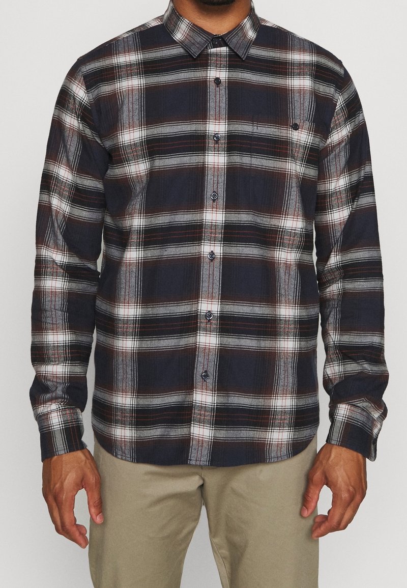 Koszula w kratę w kolorze granatowym, białym i czerwonym. Posiada kołnierzyk zapinany na guziki, długie rękawy i kieszeń z przodu. Wykonana z teksturowanej mieszanki bawełny.