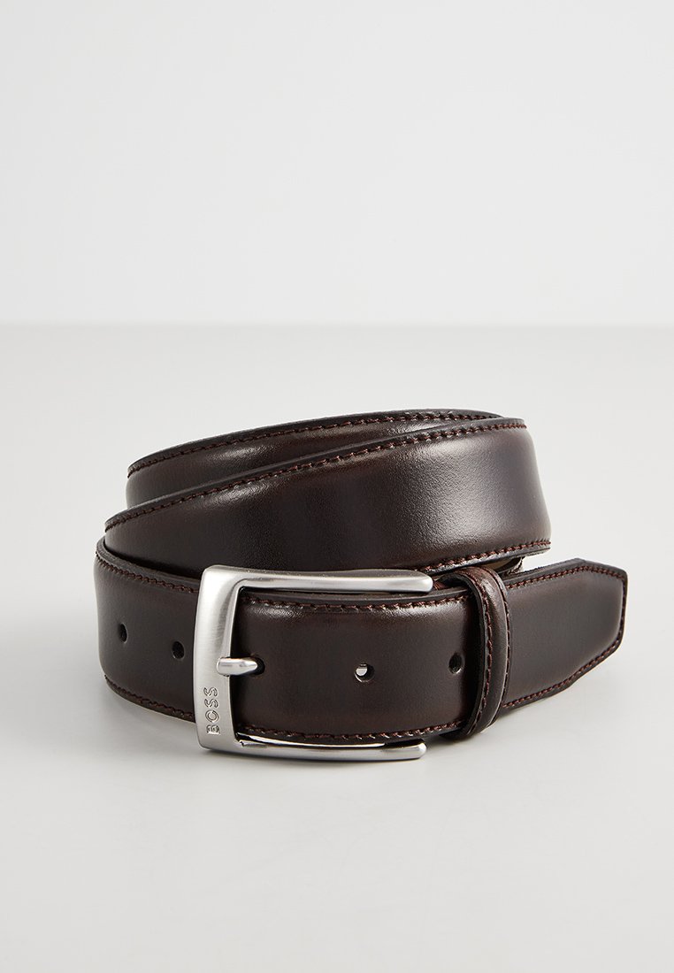 Bruine leren riem met een gladde afwerking, zilveren metalen gesp en subtiele stiksels langs de randen. Verstelbaar met meerdere gaatjes.