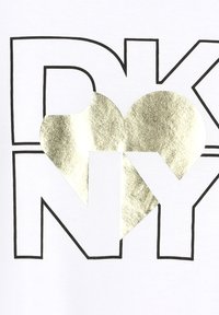 Camiseta blanca con letras negras en negrita "DKNY" y una gran forma de corazón metálico dorado integrada entre la "D" y la "K". Textura suave.