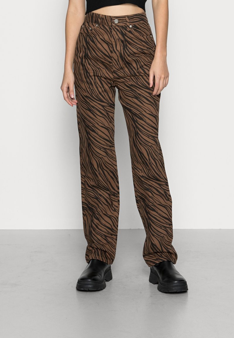 Pantaloni marroni con un motivo a strisce di tigre nere, vita alta, vestibilità ampia e design a cinque tasche. Abbinati a stivali neri chunky.