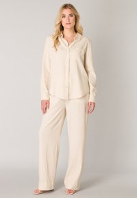 Beiges Hemd und weit geschnittene Hose aus Leinen. Das Hemd verfügt über einen Kragen, eine Brusttasche und eine Knopfleiste. Glatter, leichter Stoff.