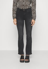 Svarta utsvängda jeans med framfickor, slitna detaljer och slim fit, tillsammans med svarta platåsandaler. Djurmönstrad topp synlig.