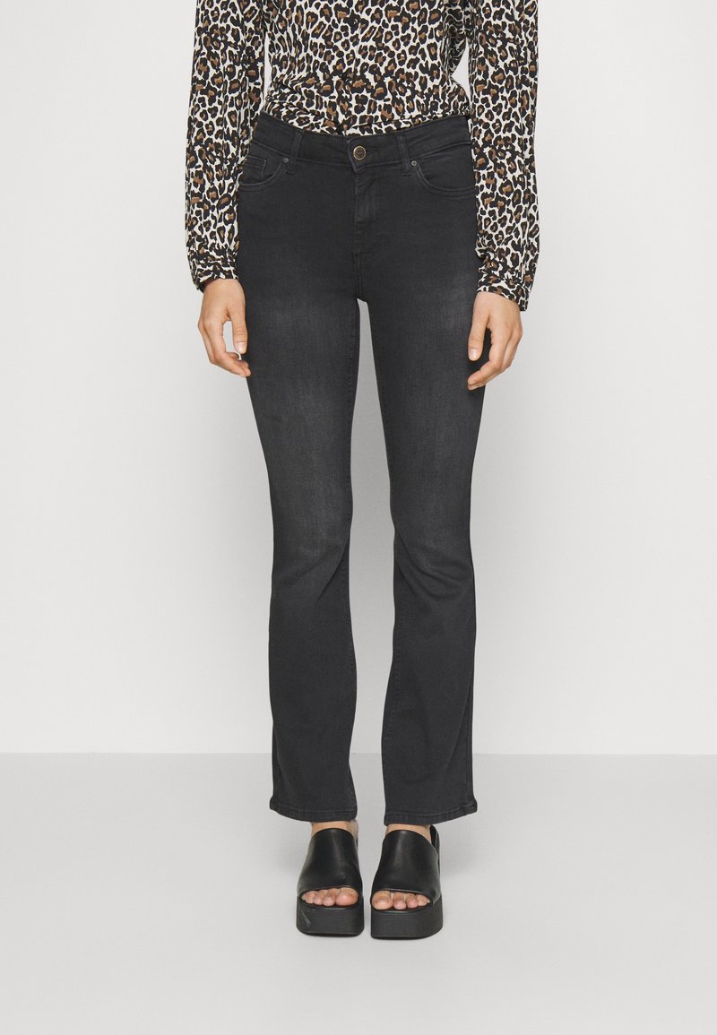 Svarta utsvängda jeans med framfickor, slitna detaljer och slim fit, tillsammans med svarta platåsandaler. Djurmönstrad topp synlig.