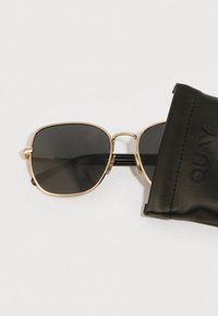 Päikeseprillid kuldse metallraamiga, mustade läätsedega ja ruudukujulise disainiga. Kaasas must nahast karp, millel on reljeefne tekst.