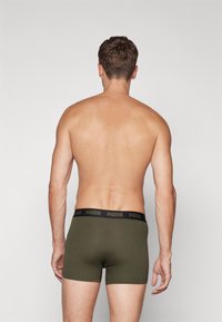 Zöld pamut boxer shorts fekete deréktartóval, amelyen a "PUMA" logó látható, egy férfi modellen hátulról, semleges háttér előtt.