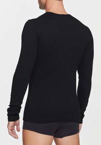 Maglietta nera a maniche lunghe realizzata in un morbido materiale elasticizzato, con scollatura rotonda e design aderente, abbinata a pantaloni corti scuri.