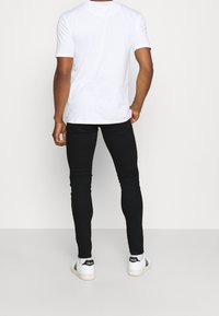 Camiseta blanca de manga corta, jeans de denim negro ajustados y zapatillas blancas con acentos negros. Enfoque en un diseño casual y contemporáneo.