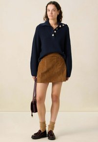 Pull en maille côtelée bleu marine avec un grand col, mini-jupe en daim marron avec deux poches avant, chaussettes texturées beige et chaussures noires.