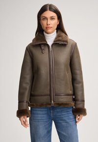 Bruine leren jas met een zachte bontkraag en manchetten, voorzien van zijzakken en contrasterende donkerbruine accenten. Ritssluiting aan de voorkant.