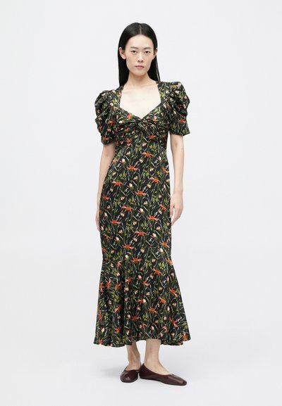 Robe florale avec des manches bouffantes, fond noir avec des motifs rouges et verts, corsage ajusté, jupe fluide, associée à des ballerines sombres.