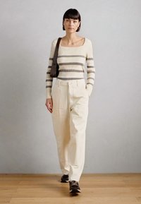 Cream and gray striped knitted sweater, beige wide-leg trousers, brown handbag, and dark sneakers. Simple, relaxed silhouette. Wood flooring backdrop.