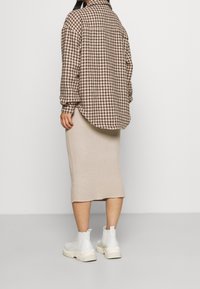 Hnědá a béžová košile s dlouhým rukávem ve vzoru houndstooth, zkombinovaná s béžovou žebrovanou midi sukni a bílými silnými kotníkovými botami.