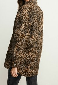 Leopard print shirt in brown and black, featuring a collared design, long sleeves, and buttoned cuff detail. Soft fabric with a relaxed fit.