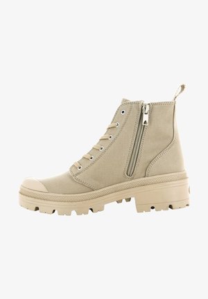 Bottines en toile beige avec un capuchon en caoutchouc, lacets sur le devant, fermeture éclair sur le côté et semelle en caoutchouc texturée pour une meilleure adhérence.