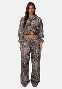 Korte camouflage hoodie en bijpassende brede broek in bruin- en grijstinten. Zachte stof met een bosachtige textuur en bladerenpatroon.