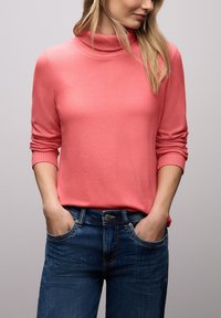 Różowy sweter z golfem o prążkowanym kołnierzu, długich rękawach i luźnym kroju. Połączony z niebieskimi jeansami o klasycznym, pięciokieszeniowym fasonie.