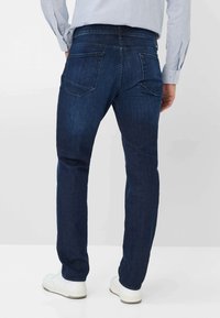 Donkerblauwe denim jeans met een recht model, voorzien van twee achterzakken en minimale stikdetails. Gedragen met witte sneakers.