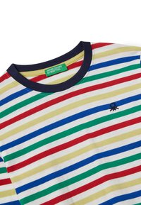 Proužkované tričko s horizontálními pruhy v červené, zelené, modré a žluté barvě na bílém pozadí. Má námořnický límec a malou logovouDetail.