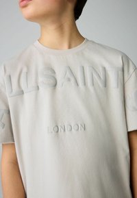 Vaaleanharmaa lyhythihainen t-paita, joka on valmistettu pehmeästä kankaasta. Paita on varustettu kohotetulla painatuksella, jossa lukee "ALLSAINTS" ja "LONDON" hienovaraisessa suunnitelmassa.