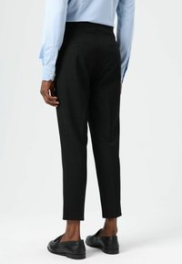 Pantalon noir sur mesure avec une coupe slim et une longueur raccourcie. Tissu lisse, poches latérales et fermeture éclair dissimulée à l'arrière. Associé à une chemise bleu clair.