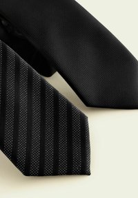 Deux cravates noires : l'une lisse et unie, l'autre avec un motif rayé et de petits points blancs. Les deux présentent un design classique de pointe triangulaire.