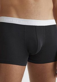 Boxer shorts en coton noir avec une ceinture élastique blanche ornée du texte "TOMMY HILFIGER" en relief. La coupe est ajustée et sans couture.