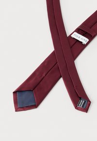 Μπορντό μεταξωτή γραβάτα με μονόχρωμο σχέδιο, με εσωτερική φόδρα σκούρου μπλε και ετικέτα επωνυμίας. Λεία υφή και κλασικό μυτερό σχήμα.