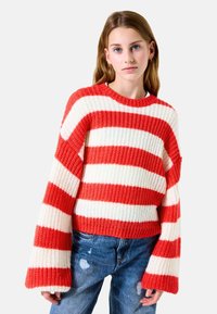 Gestreifter Pullover in Rot und Weiß mit einer groben Stricktextur, weiten Ärmeln und einem klassischen Rundhalsausschnitt, kombiniert mit distressed Jeans.
