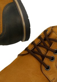 Hnědé semišové boty s tmavými gumovými podrážkami, viditelnými tkaničkami a kovovými očky. Texturované detaily na patě a bočních panelech.