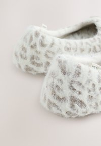 Chaussons duveteux blanc et marron clair à motif léopard avec une texture douce sur un fond neutre.