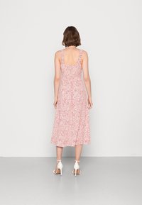 Rood en wit gestreepte midi-jurk met gerimpelde bandjes en een aansluitende bovenkant, die overloopt in een uitlopende rok. Model draagt witte hakken.