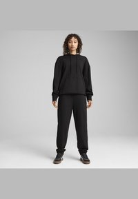 Sort hættetrøje med kængurulomme og snor, parret med matchende sorte sweatpants. Begge dele har en afslappet pasform og tekstureret stof.