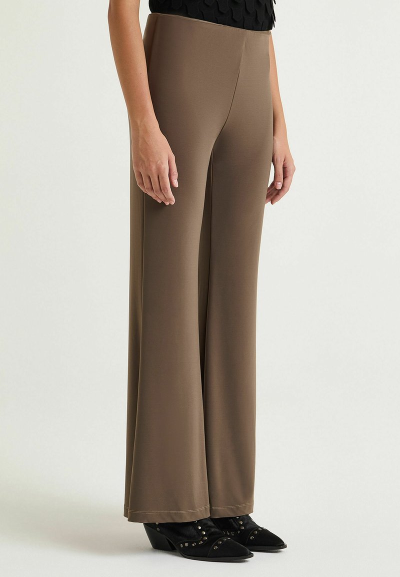 Pantaloni marroni a gamba larga realizzati in tessuto elasticizzato, con una texture liscia e una vita elasticizzata, abbinati a scarpe nere con tacco.