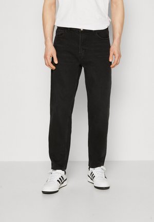 Black denim jeans with a straight cut, five-pocket design, and a slightly faded appearance, paired with white sneakers featuring black stripes.