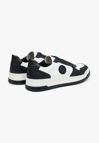 Černobílé kožené tenisky s hladkým povrchem, kulatou špičkou a strukturovanou podešví; na boku se nachází kruhové logo.