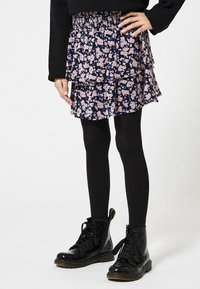 Floral printed short skirt with navy background, layered design, elastic waistband, worn over black tights and patent leather black boots.